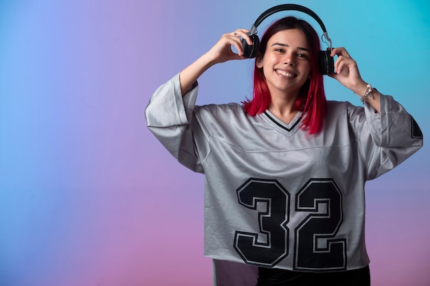 Young girl with pink hairs looks positive and wearing headphones.