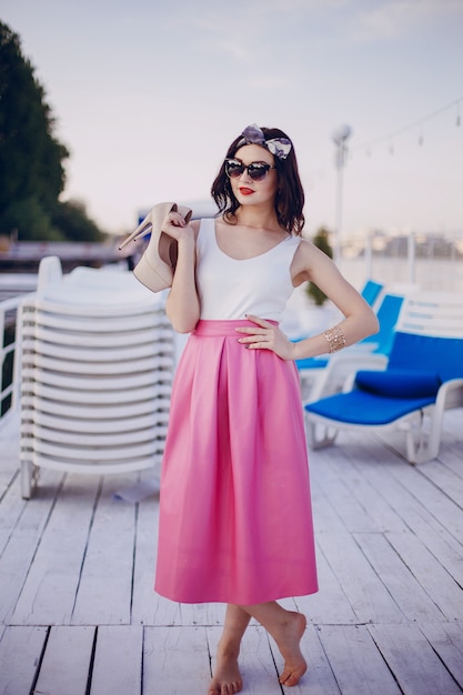 Free photo young girl with pink skirt posing with sunglasses and high heels