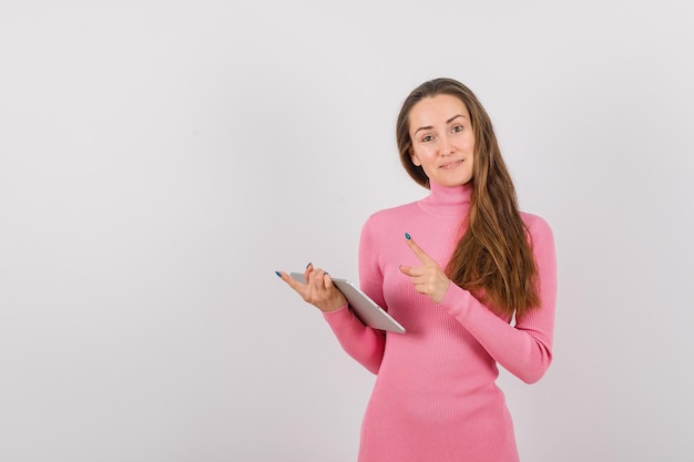 Young girl with planshet computer is pointing to left with forefinger on white background