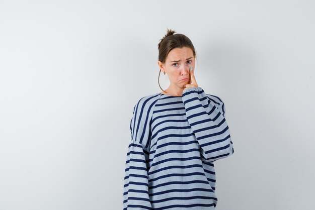 Young girl with puckering lips showing her right eye with her finger on white background