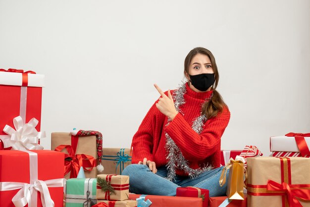 young girl with red sweater and black mask sitting around presents on white