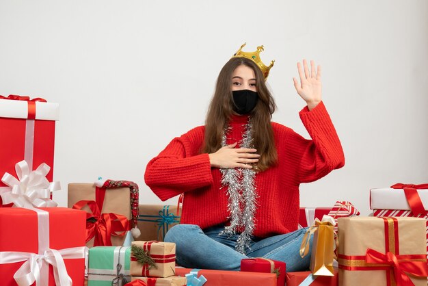 young girl with red sweater and crown sitting around presents with black mask on white