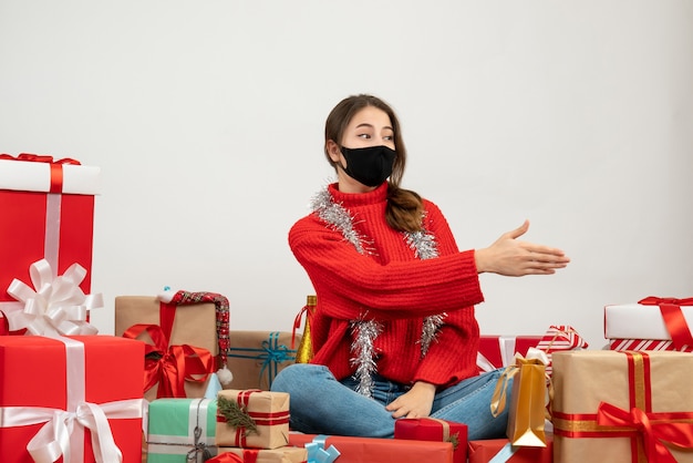 Giovane ragazza con maglione rosso che dà mano seduto intorno presenta con maschera nera su bianco