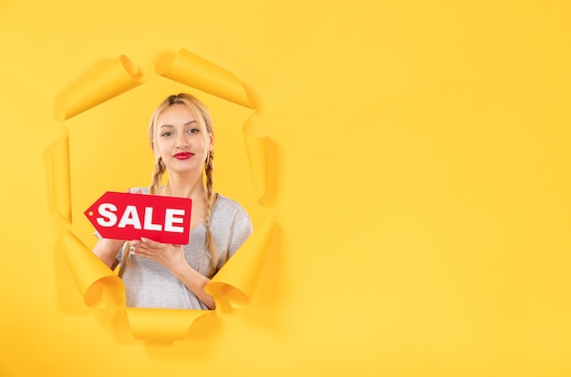 Free photo young girl with sale inscription sign on a torn yellow background fashion shopping indoor