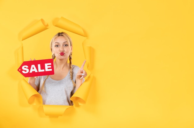 Foto gratuita giovane ragazza con il segno dell'iscrizione di vendita sullo sfondo giallo strappato per lo shopping facciale al coperto