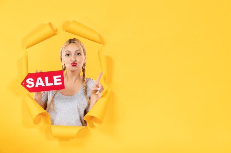 Бесплатный Фотография молодая девушка с надписью "продажа" на рваном желтом фоне делает покупки для лица в помещении