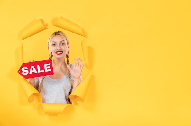 Молодая девушка с надписью "Продажа" на рваном желтом фоне делает покупки на лице в помещении
