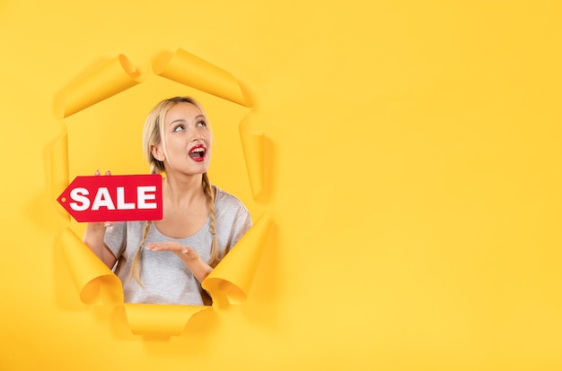 Young girl with sale inscription sign on torn yellow surface indoor facial shopping