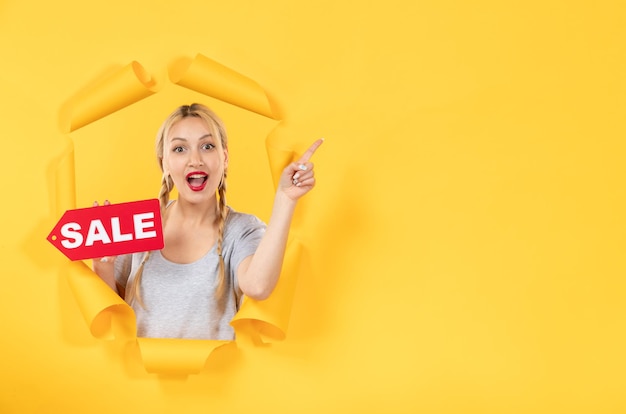 Free photo young girl with sale inscription sign on the torn yellow surface