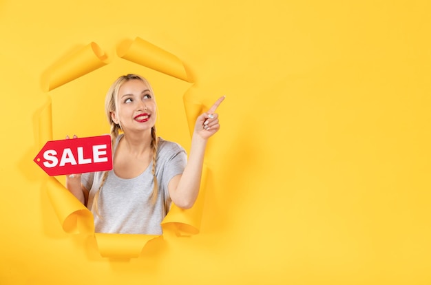 Young girl with sale inscription sign on torn yellow surface