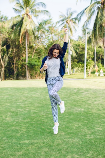 Young girl with short dark hair jumping in the park with palms