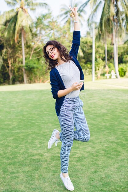 Young girl with short dark hair jumping in the park with palms