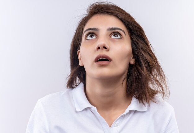 Young girl with short hair wearing white polo shirt looking up surprised 