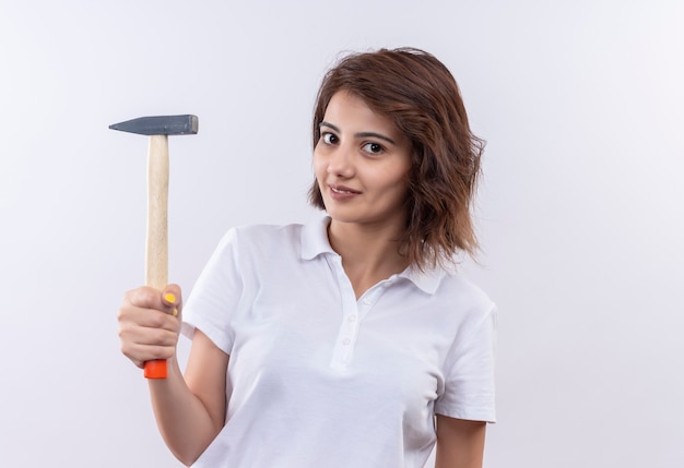 Young girl with short hair wearing white polo shirt smiling confident holding hammer 