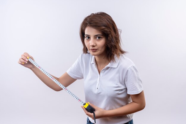 Young girl with short hair wearing white polo using measure tape looking at camera with confident look 