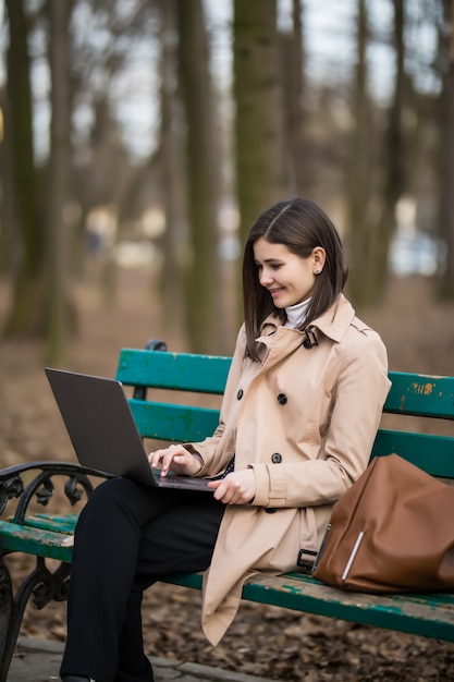 Young girl working in park on a bench with laptop