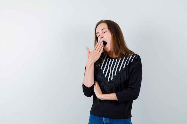 Young girl yawning and covering her mouth with her hands on white background