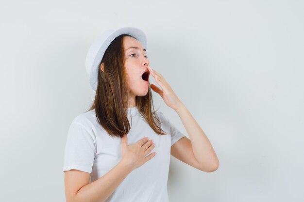 Young girl yawning in white t-shirt hat and looking sleepy  