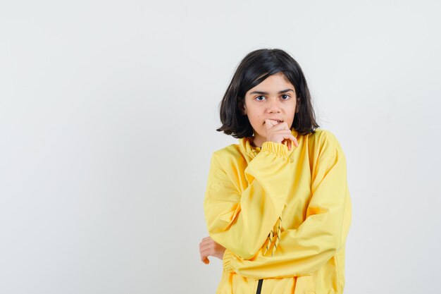 Young girl in yellow bomber jacket biting fingers and thinking about something and looking pensive