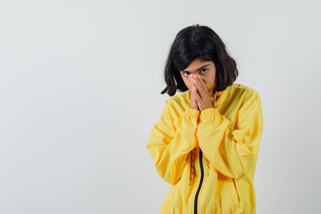 Free photo young girl in yellow bomber jacket covering mouth with hands and looking timid