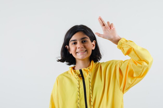 Young girl in yellow bomber jacket showing gun gesture and looking happy