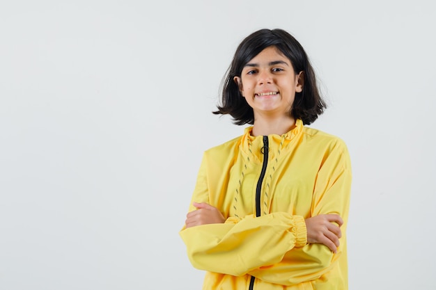 Young girl in yellow bomber jacket standing arms crossed and looking happy