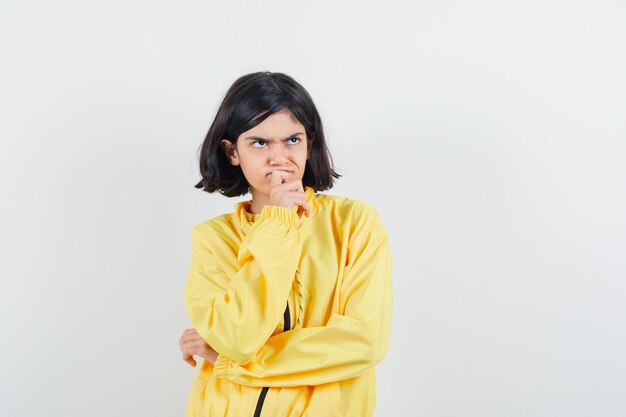 Young girl in yellow bomber jacket standing in thinking pose and looking pensive