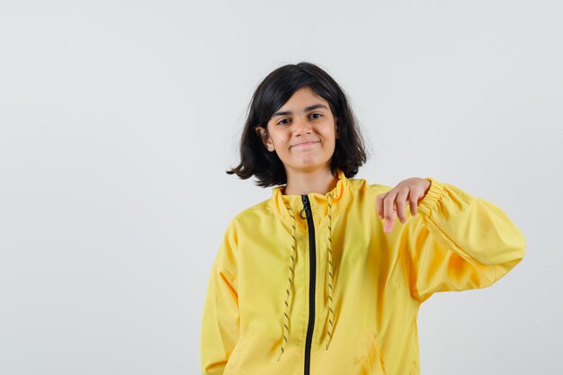 Young girl in yellow bomber jacket stretching hand as holding something and looking happy