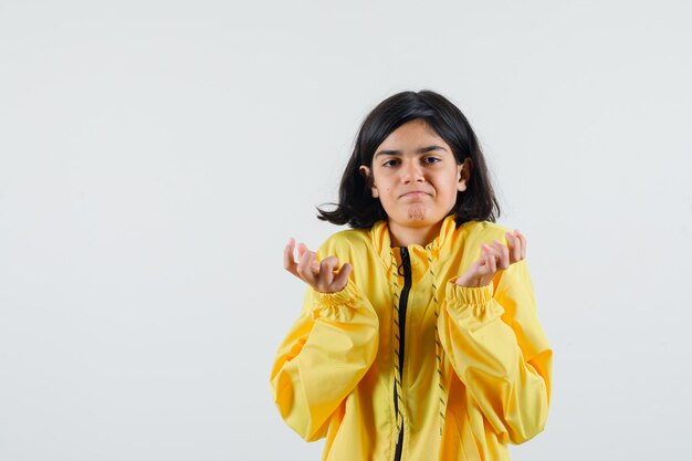 Young girl in yellow bomber jacket stretching palms as holding something and looking serious