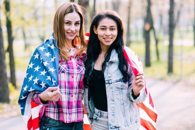 Free photo young girlfriends wrapping in american flag standing outside