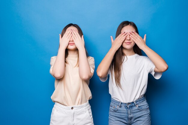 Young girls covering eyes by hands isolated on blue wall