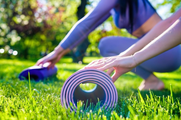 Young girls dressed in yoga clothes holding their eco friendly yoga mats on the green grass