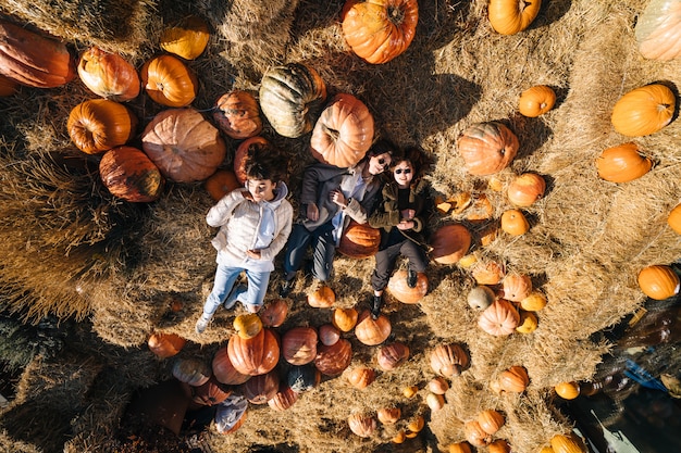 Young girls lie on haystacks among pumpkins. View from above