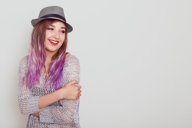 Young good looking girl with violet hair, expressing love, hugging herself, looking away with dreamy expression, copy space for advertisement, isolated over grey background.