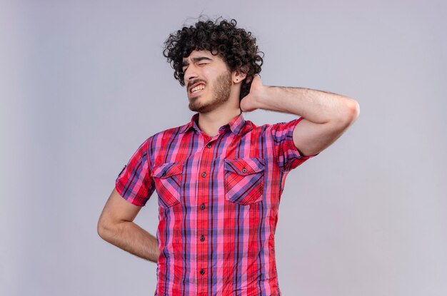 A young good-looking man with curly hair in checked shirt keeping hand on head and feeling bad 