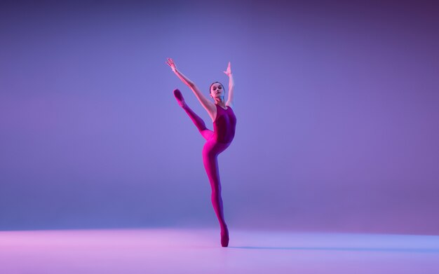 ネオンの光の中で紫色のスタジオの背景に分離された若くて優雅なバレエダンサー