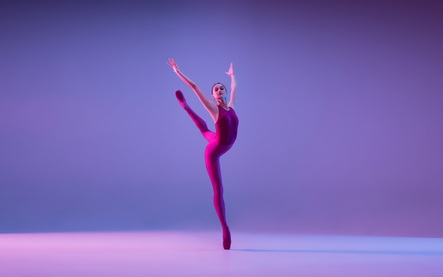 Young and graceful ballet dancer isolated on purple studio background in neon light