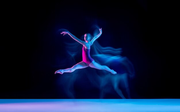 네온 불빛에 보라색 스튜디오 배경에 고립 된 젊고 우아한 발레 댄서