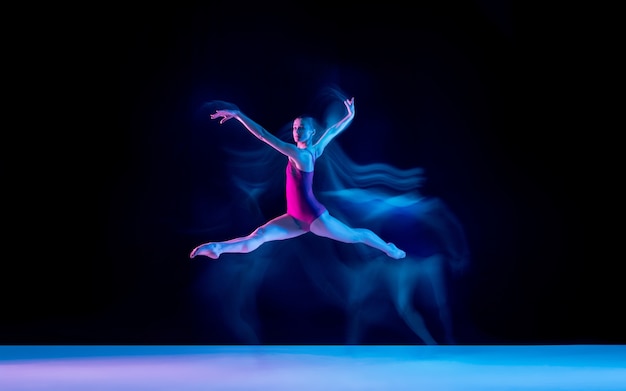 네온 불빛에 보라색 스튜디오 배경에 고립 된 젊고 우아한 발레 댄서