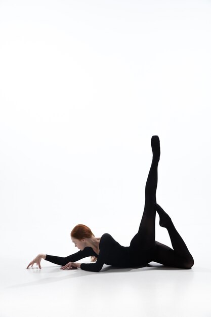白いスタジオの背景に分離された最小限の黒のスタイルで若くて優雅なバレエダンサー。