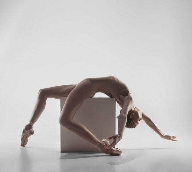 Young graceful female ballet dancer or classic ballerina dancing on white studio.