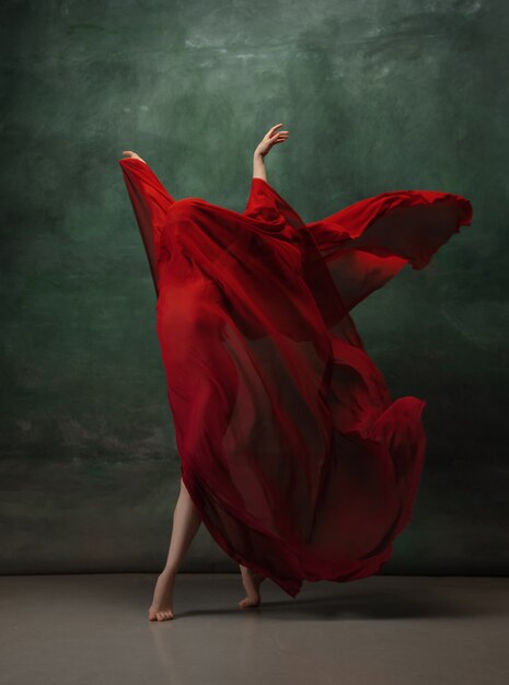 Young graceful tender ballerina on dark green studio space with red cloth