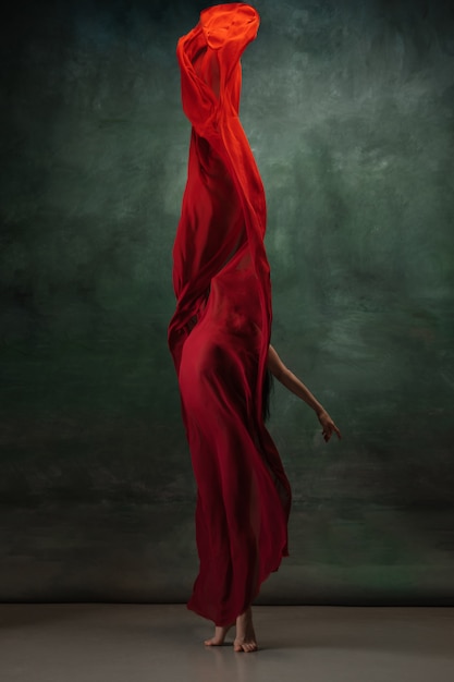 Young graceful tender ballerina on dark green studio space with red cloth