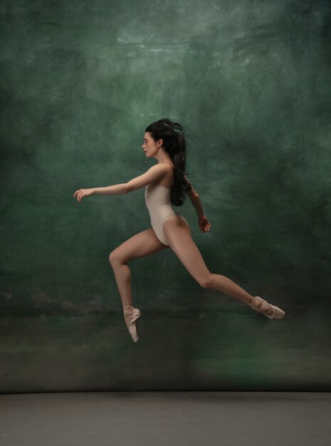 Молодая изящная нежная балерина на темно-зеленом пространстве студии