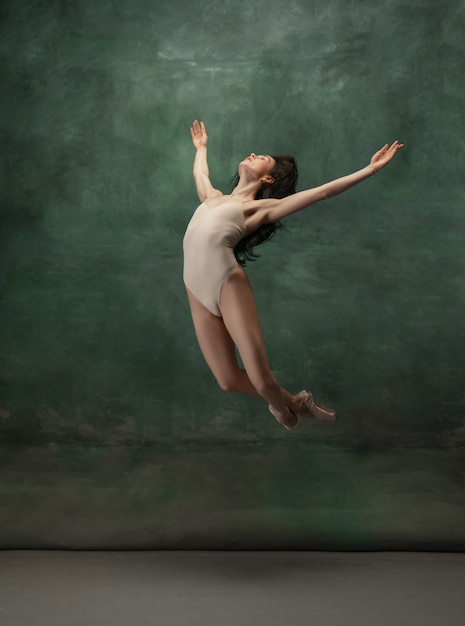 Молодая изящная нежная балерина на темно-зеленом пространстве студии