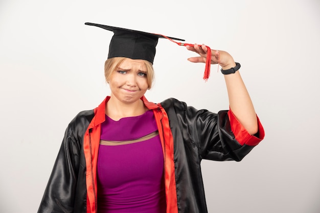 Young graduate student in gown looking at camera on white.