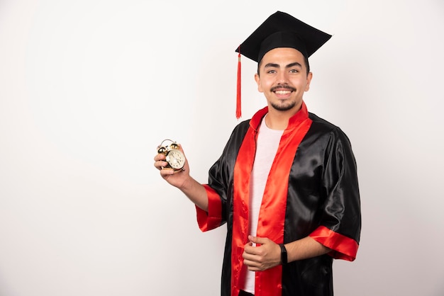 Young graduate student holding clock on white.