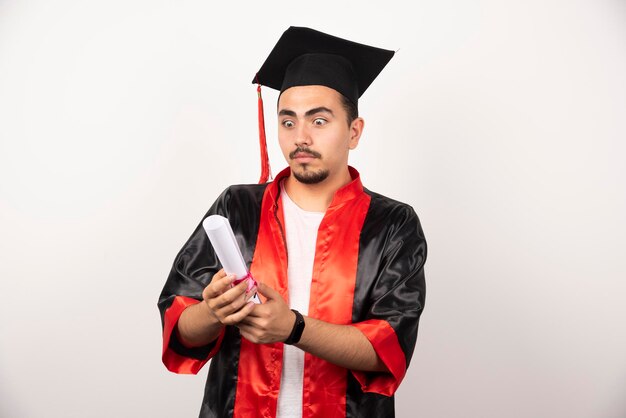 Young graduate student looking baffled at diploma on white.