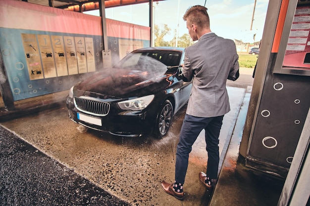 Young groomed man is washing his own car at car washing station.