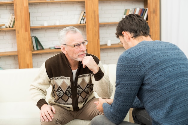 Free photo young guy and aged concentrated man on sofa in room